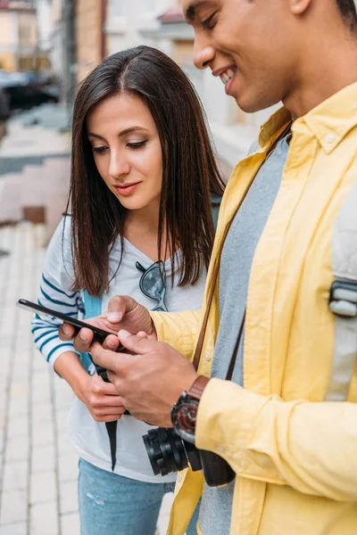 Привлекательная девушка смотрит на смартфон рядом с красивым смешанной расы мужчина — стоковое фото