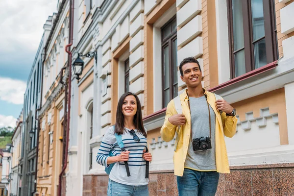 Glückliches Mädchen berührt Rucksack beim Spazierengehen mit Mischling in der Nähe von Gebäuden in der Stadt — Stockfoto