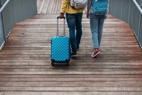 Cropped view of multicultural man and woman walking with blue luggage — Stock Photo