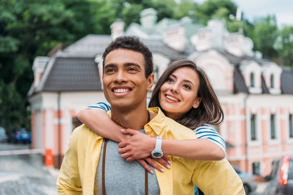 Счастливая девушка обнимает красивого мужчину смешанной расы рядом со зданием — стоковое фото