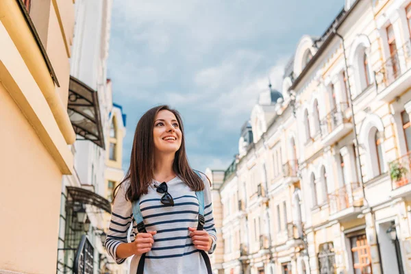 Низкий угол обзора счастливой девушки с рюкзаком возле зданий — стоковое фото