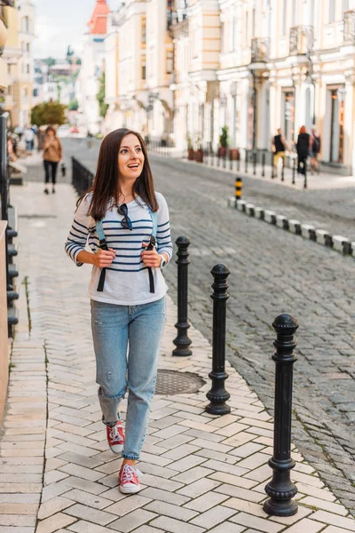 Счастливая молодая женщина ходит с рюкзаком возле зданий — стоковое фото