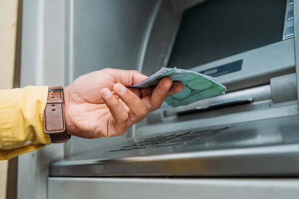 Vista recortada del hombre de raza mixta tomando dinero de la máquina del cajero automático - foto de stock