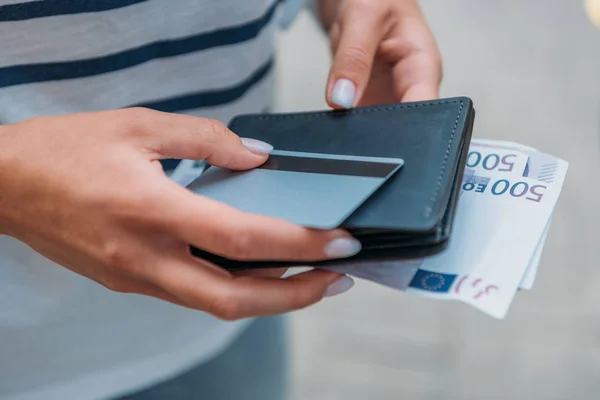 Обрезанный вид женщины, держащей банкноты евро и кредитную карту с кошельком — стоковое фото