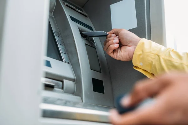 Vista recortada del hombre bi-racial poniendo tarjeta de crédito en el cajero automático - foto de stock