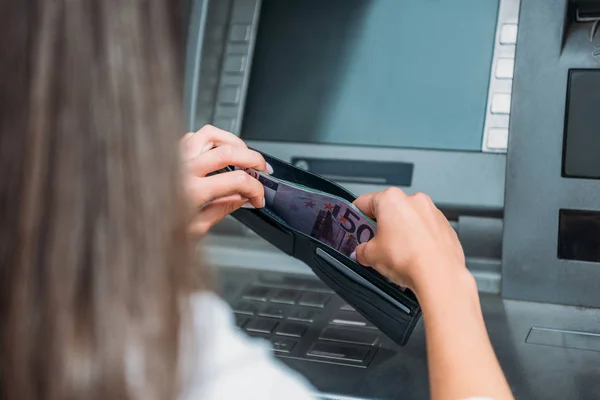 Vista recortada de la mujer poniendo dinero en la cartera cerca de cajero automático - foto de stock