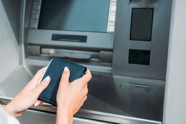 Vista recortada de la mujer sosteniendo la cartera cerca de cajero automático - foto de stock