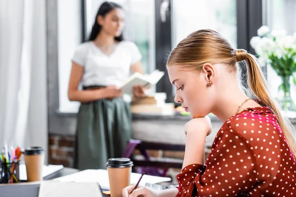 Selective focus of blonde student in blouse writing with pencil — Stock Photo