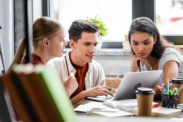 Focus selettivo di studenti multietnici che sorridono e guardano laptop in appartamento — Foto stock