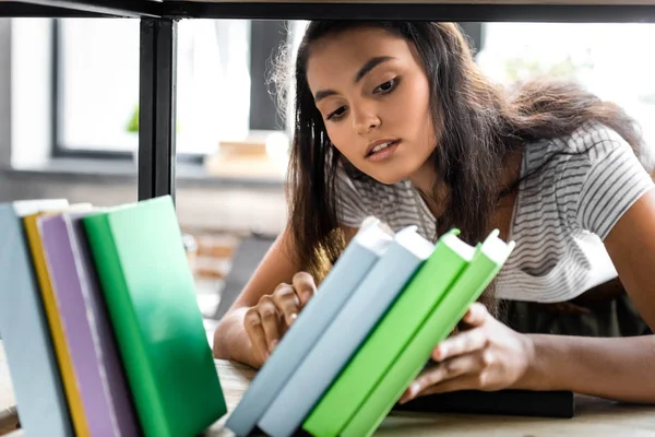 Selective focus of bi-racial student holding books in apartment — Stock Photo