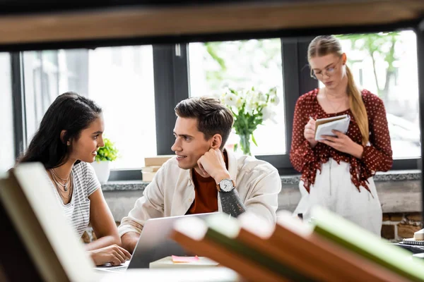 Étudiants multiethniques souriant et se regardant dans l'appartement — Photo de stock