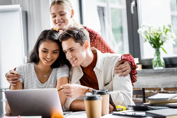 Multiethnic students smiling and looking at laptop in apartment — Stock Photo