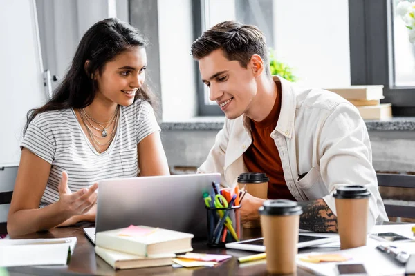 Studenti multietnici sorridenti e guardando il computer portatile in appartamento — Foto stock