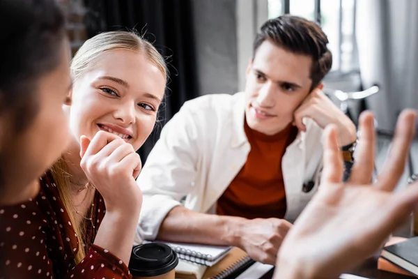 Enfoque selectivo de los estudiantes multiétnicos sonriendo y hablando en apartamento - foto de stock