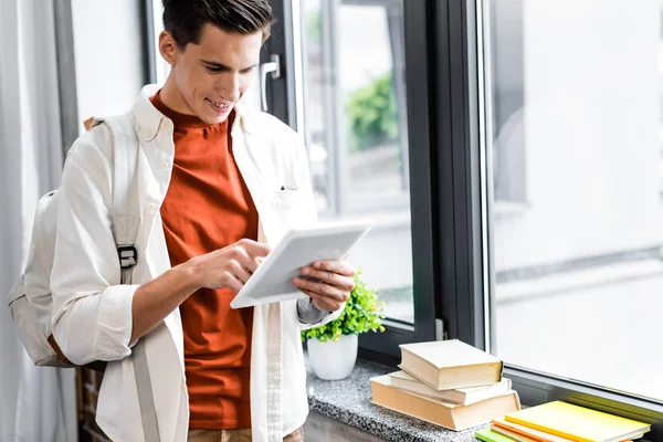 Beau étudiant souriant et utilisant une tablette numérique dans l'appartement — Photo de stock