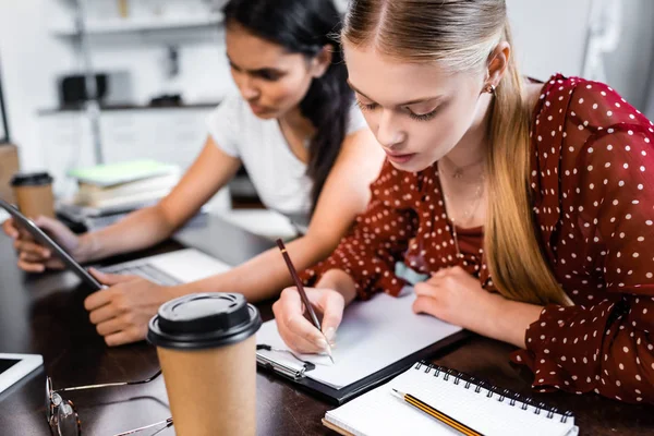 Selective focus of multicultural friends writing and using laptop — Stock Photo