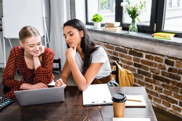 Attraktive multikulturelle Freunde, die in der Wohnung lächeln und auf den Laptop schauen — Stockfoto