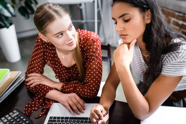 Attractive and multicultural friends looking at laptop in apartment — Stock Photo