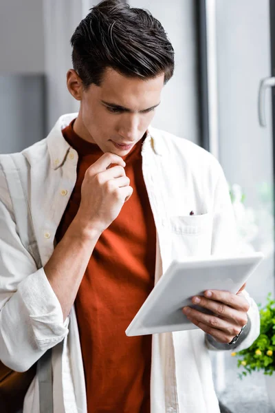 Beau étudiant en chemise en utilisant une tablette numérique dans l'appartement — Photo de stock