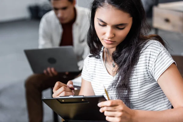 Attractive and bi-racial student writing with pencil in apartment — Stock Photo