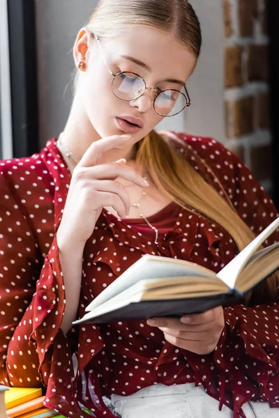Attrayant étudiant en lunettes et chemisier livre de lecture dans l'appartement — Photo de stock