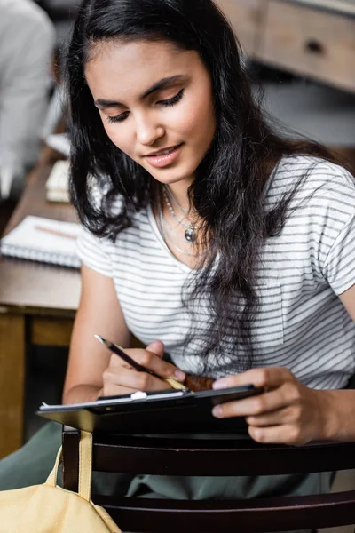 Attraktive und bi-rassische Studentin mit Klemmbrett und Bleistift in der Wohnung — Stockfoto