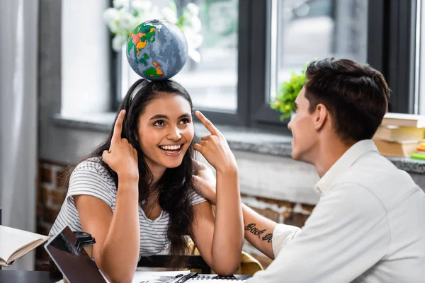 Bi-racial student pointing with fingers at globe and smiling with friend — Stock Photo