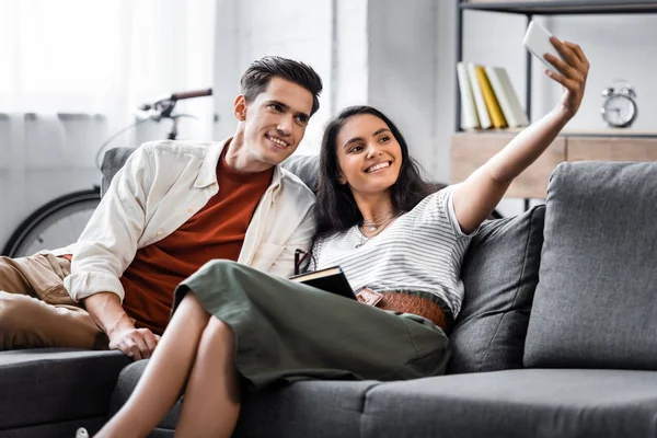 Happy multicultural students smiling and taking selfie in apartment — Stock Photo