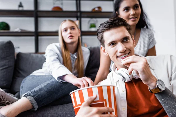 Focus selettivo di amici multiculturali che sorridono e mangiano popcorn in appartamento — Foto stock