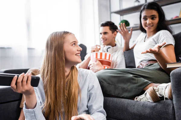 Selektiver Fokus multikultureller Freunde, die in der Wohnung lächeln und Popcorn essen — Stockfoto