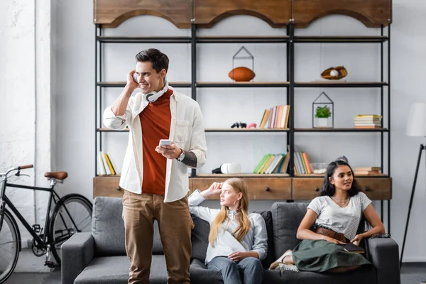 Amigos multiculturales escuchar música y sentarse en el sofá en el apartamento - foto de stock