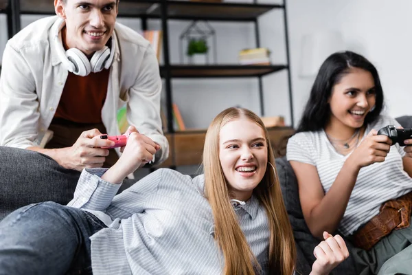 KYIV, UKRAINE - JULY 10, 2019: multicultural friends sitting on sofa and playing video game in apartment — Stock Photo