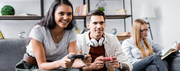 KYIV, UKRAINE - 10 JUILLET 2019 : prise de vue panoramique d'amis multiculturels jouant à des jeux vidéo en appartement — Photo de stock