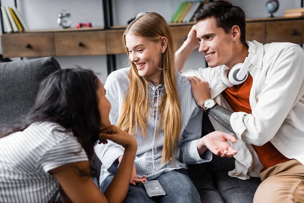 Handsome and attractive multicultural friends smiling and talking in apartment — Stock Photo