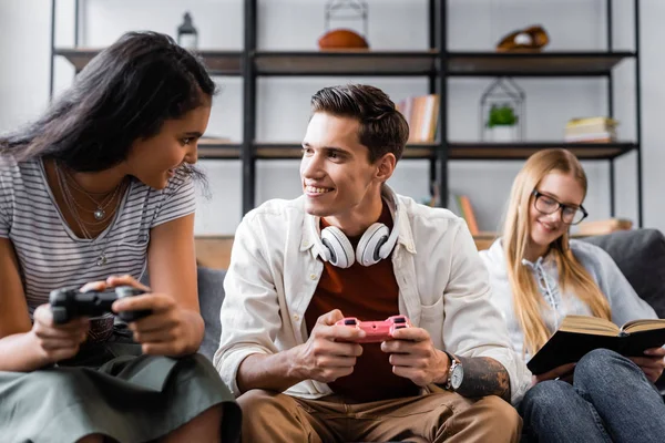 KYIV, UKRAINE - JULY 10, 2019: multicultural friends sitting on sofa and playing video game in apartment — Stock Photo
