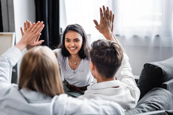 Selective focus of multicultural friends showing high five gesture in apartment — Stock Photo