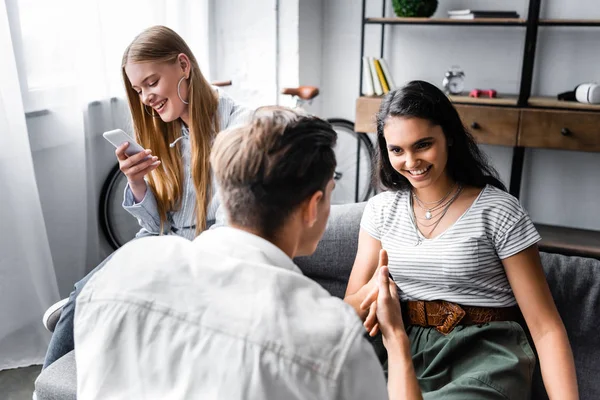 Enfoque selectivo de amigos multiculturales sonriendo y hablando en apartamento - foto de stock