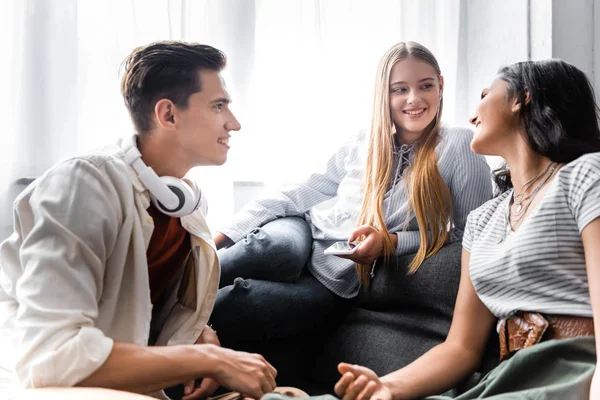 Guapos y atractivos amigos multiculturales sonriendo y hablando en apartamento - foto de stock