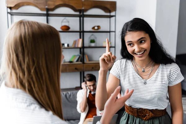Enfoque selectivo de amigos multiculturales sonriendo y hablando en apartamento - foto de stock