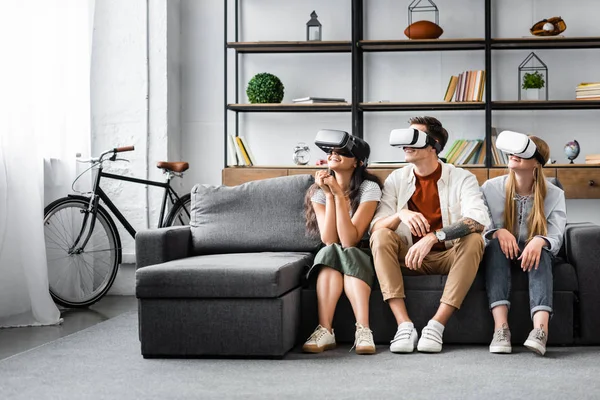 Smiling multicultural friends with virtual reality headsets sitting on sofa — Stock Photo