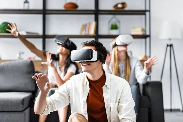 Enfoque selectivo de amigos multiculturales con auriculares de realidad virtual sentados en el sofá - foto de stock