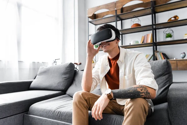 Homme avec casque de réalité virtuelle assis sur le canapé dans l'appartement — Photo de stock