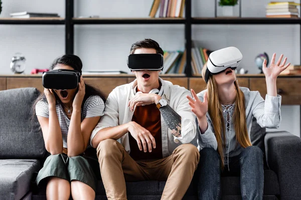 Amigos multiculturales con auriculares de realidad virtual sentados en el sofá - foto de stock