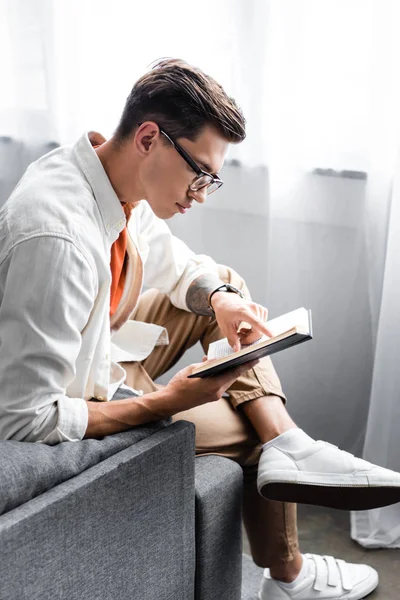 Side view of man in glasses reading book in apartment — Stock Photo