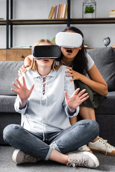 Amigos multiculturales con auriculares de realidad virtual sentados en el suelo - foto de stock