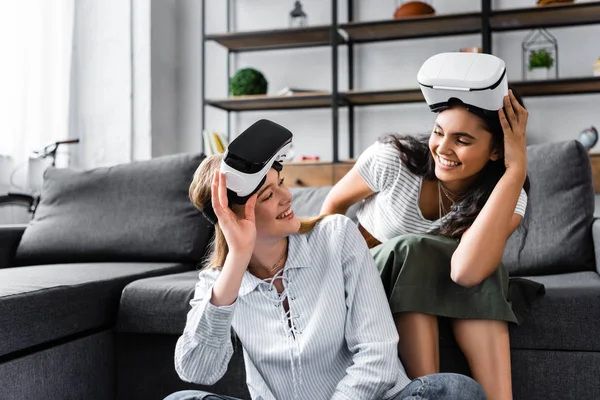 Amigos multiculturales con auriculares de realidad virtual sonriendo y mirándose - foto de stock