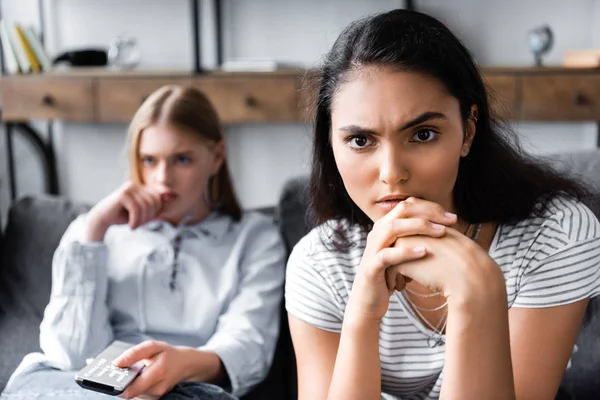 Amici multiculturali che tengono il telecomando e distolgono lo sguardo in appartamento — Foto stock