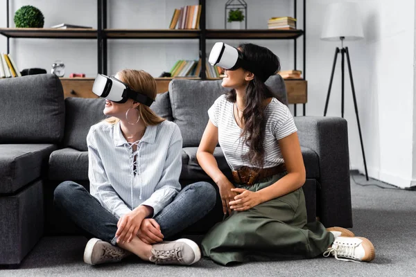 Amigos multiculturales con auriculares de realidad virtual sentados en el piso en el apartamento - foto de stock