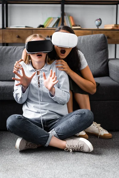 Amigos multiculturais com fones de ouvido de realidade virtual sentados no chão em apartamento — Fotografia de Stock