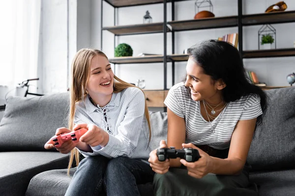 KYIV, UCRANIA - 10 de julio de 2019: amigos multiculturales sentados en el sofá y jugando videojuegos en el apartamento - foto de stock